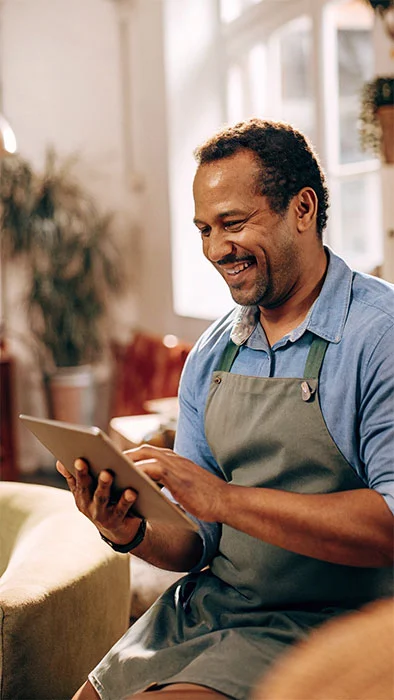 man in an apron sitting down, happily checking his ipad